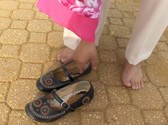Photo shows Nanta's shoes full of sand -- she is holding one of them.  the shoes are designed with two circles on the toes,and a feathered border around the entire shoe, from toes to heel and back.